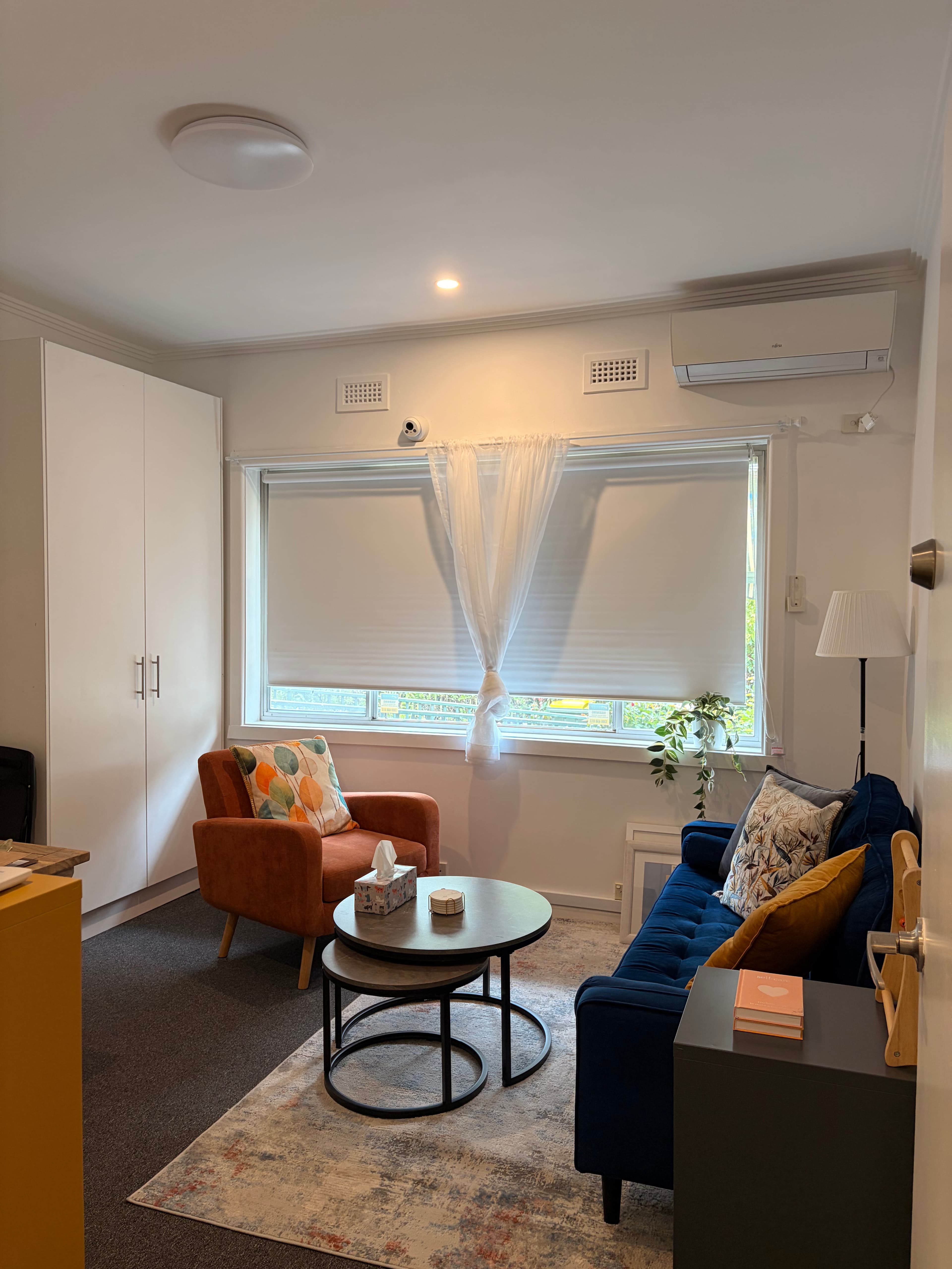 The consulting room at Brain Helpers — soft natural light from the window, an orange armchair, a rug, and a small round table where activities happen.