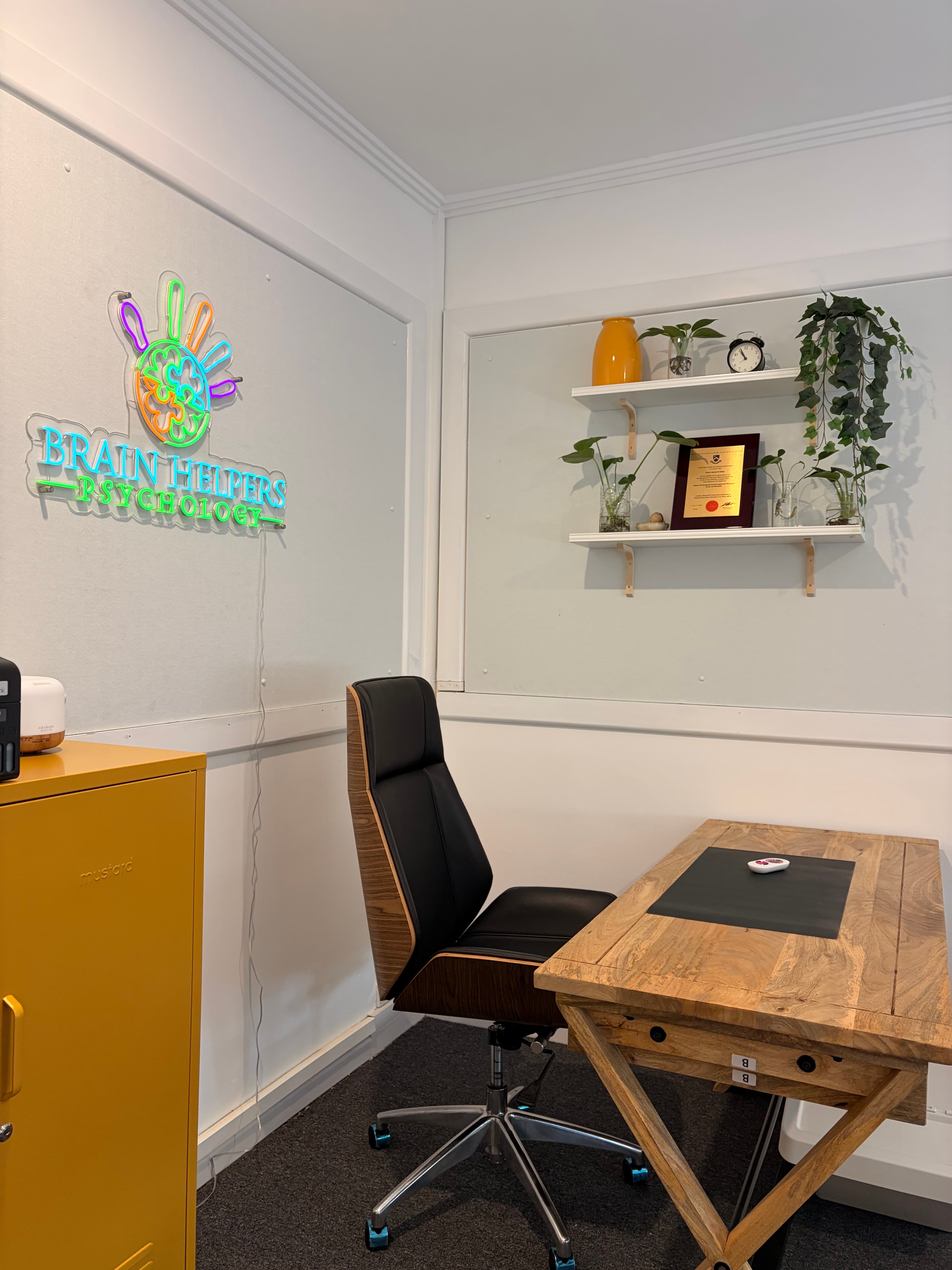 Another part of the clinic — a comfortable space with plants, a chair, and the colourful Brain Helpers logo on the floor.