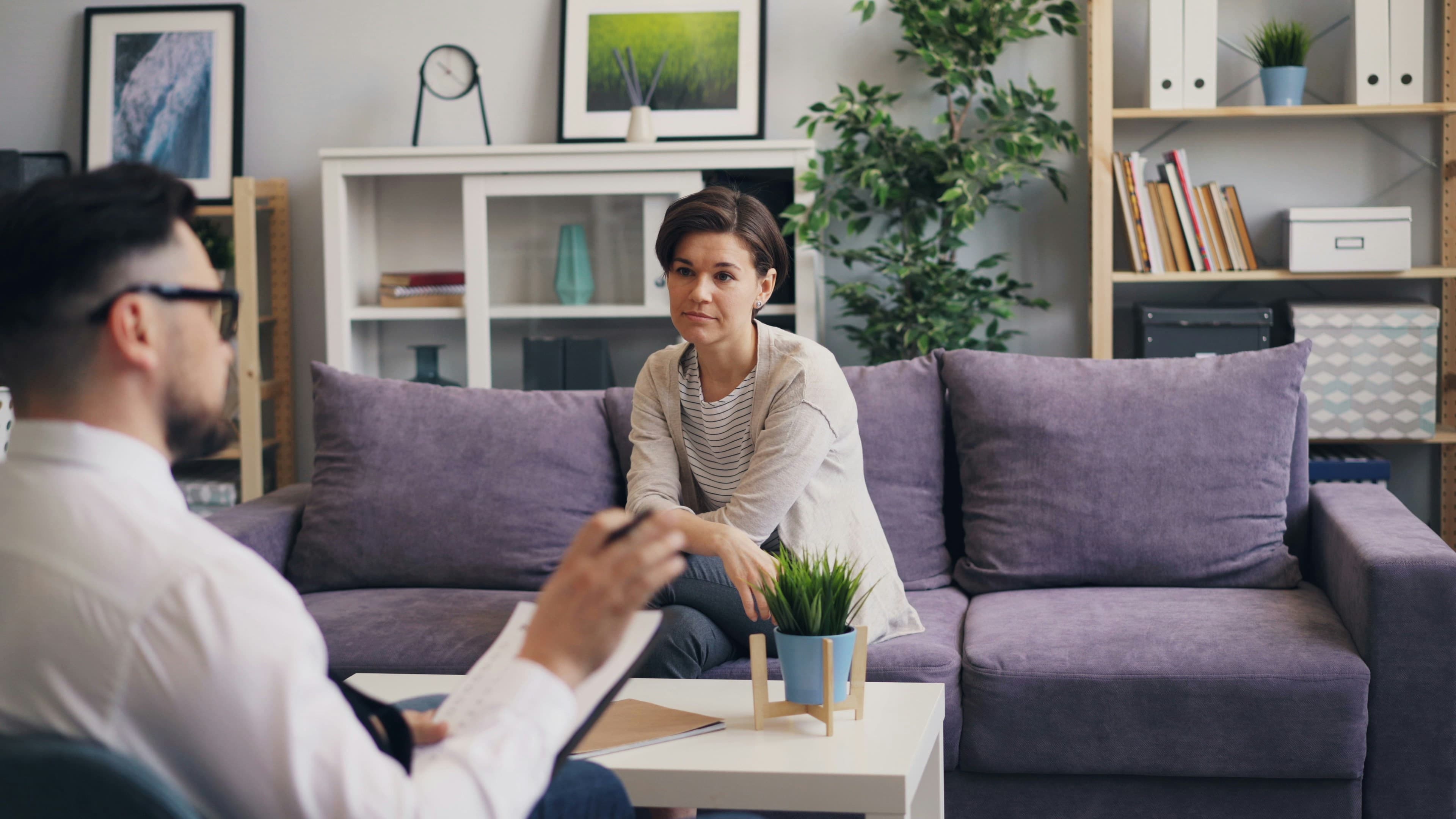 A counselling session in a warm, light-filled room — a therapist taking notes while a client speaks