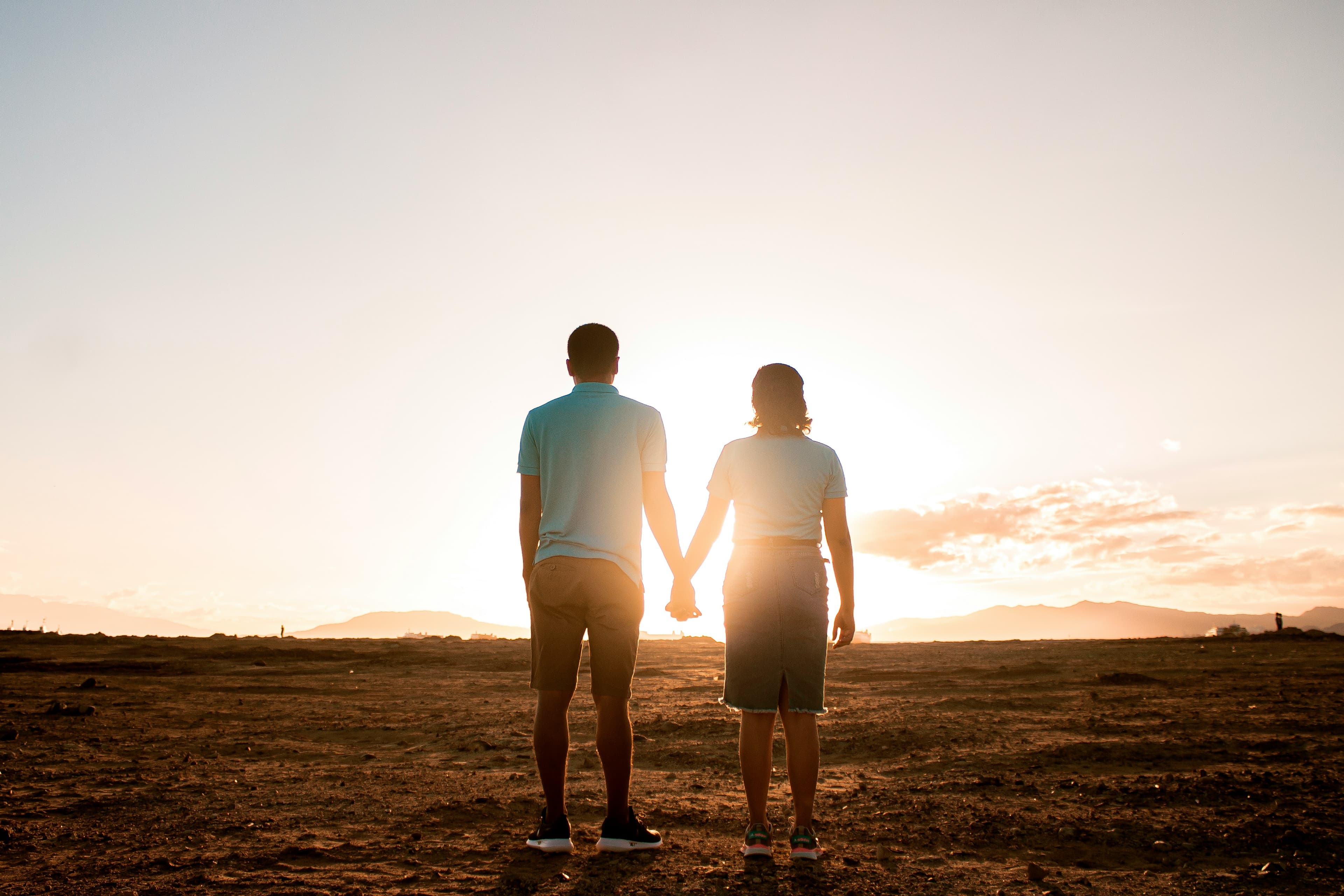 A couple holding hands at sunset, facing the horizon together